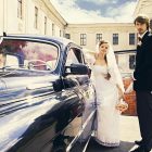 Beautiful happy young bride and groom standing near a retro auto