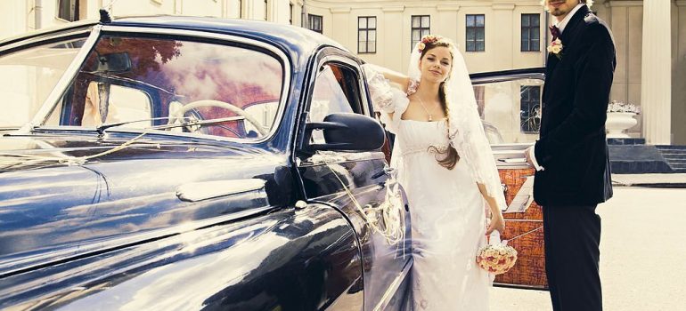 Beautiful happy young bride and groom standing near a retro auto