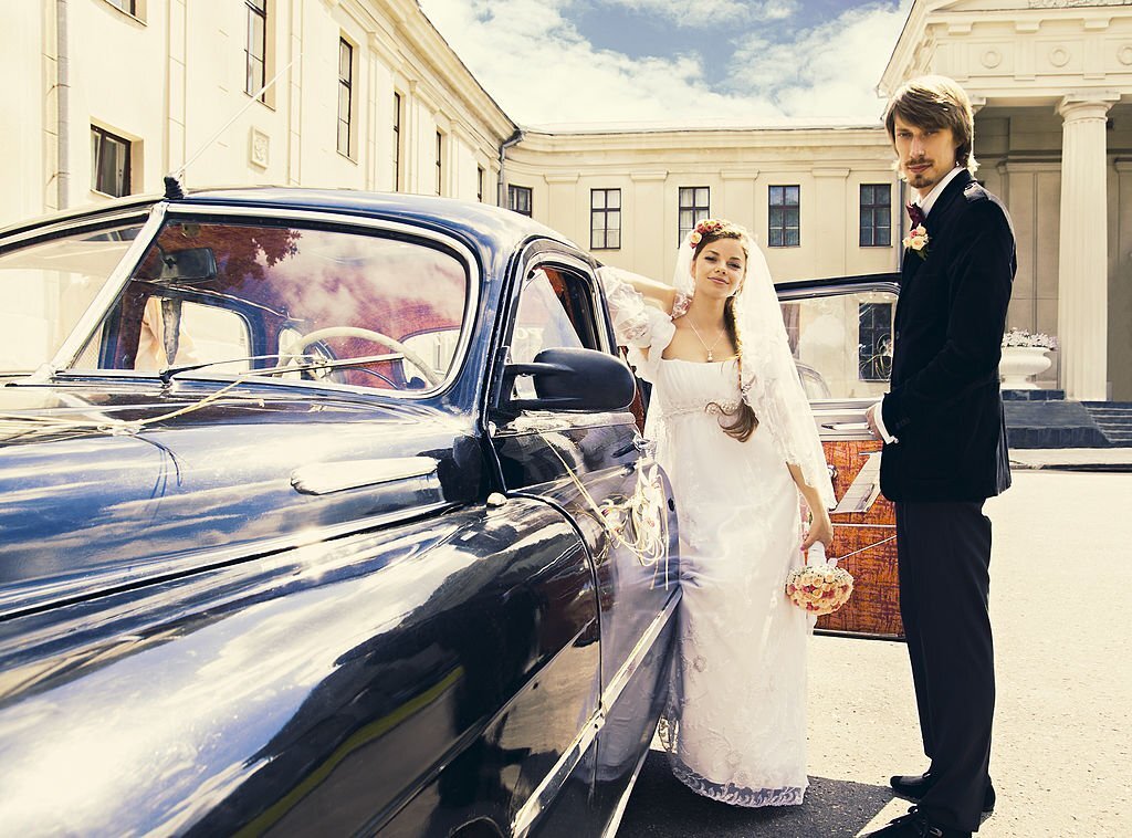 Beautiful happy young bride and groom standing near a retro auto